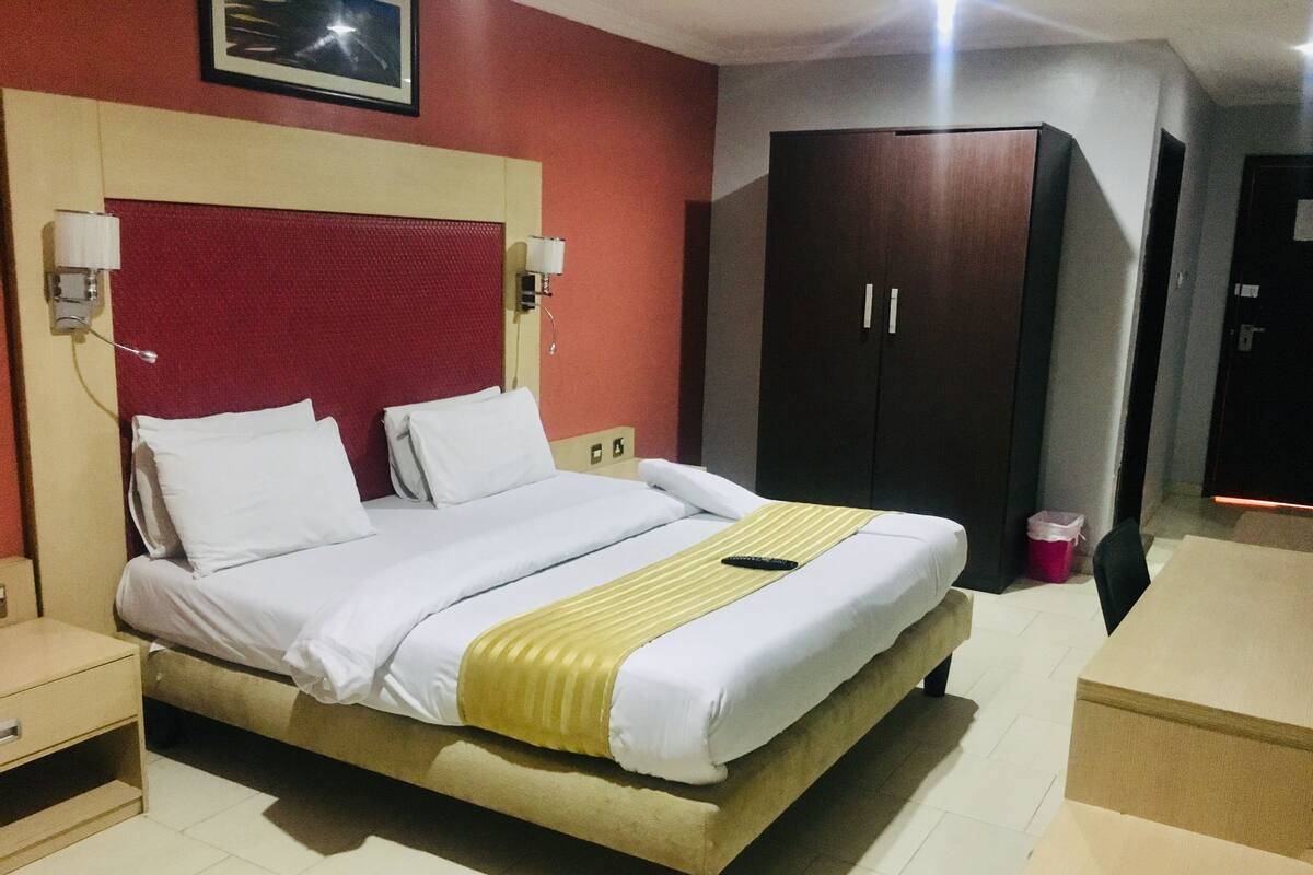 A hotel room with a bed, bedside tables, a wardrobe, and a desk.