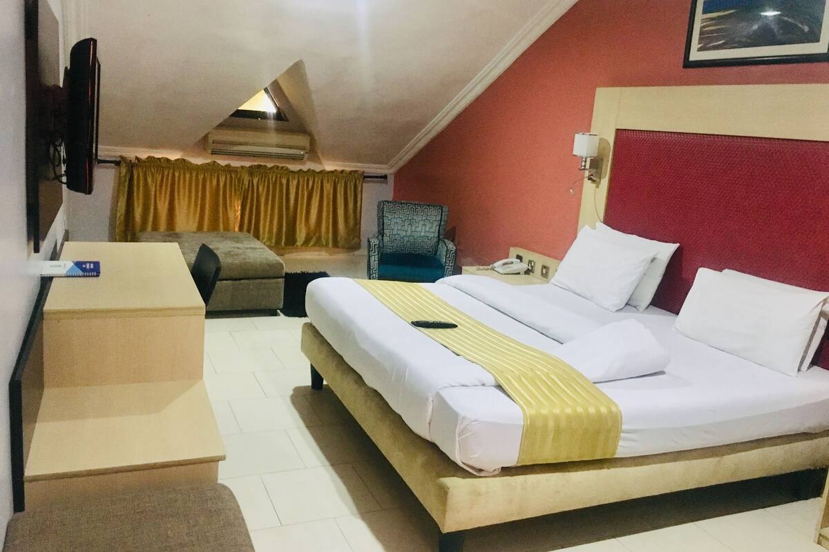 A hotel room with a bed, a desk, a chair, a TV, and a telephone.
