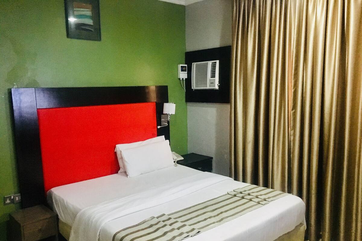 A hotel room with a red headboard, a white bedspread, and a striped throw blanket.