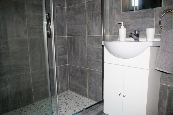 A bathroom with a glass-enclosed shower, a white sink with a mirror above it, and a towel hanging on the wall. - Blue Home (Limassol)