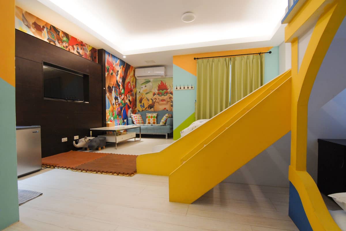 A brightly colored living room with a yellow staircase, a flat-screen TV mounted on a dark cabinet, and a colorful mural on the wall.