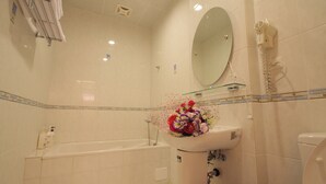 A bathroom with a bathtub, a sink with a floral arrangement, a mirror, and a hairdryer on the wall. - Staring East B & B (Hualien City)
