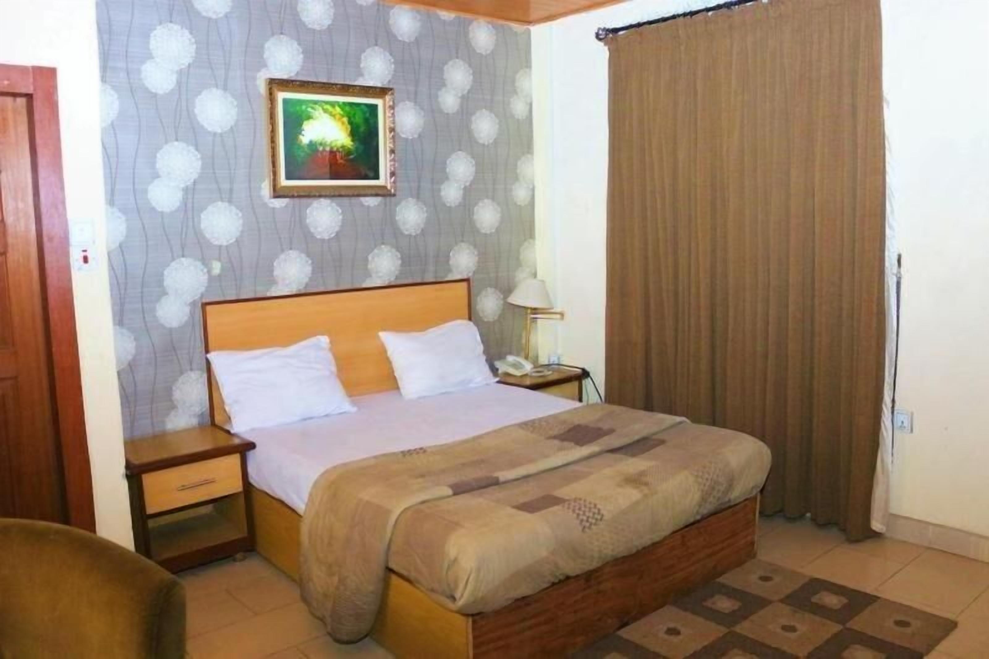 A neatly arranged bedroom with a wooden bed, a nightstand, a bedside lamp, and a framed picture on the wall.