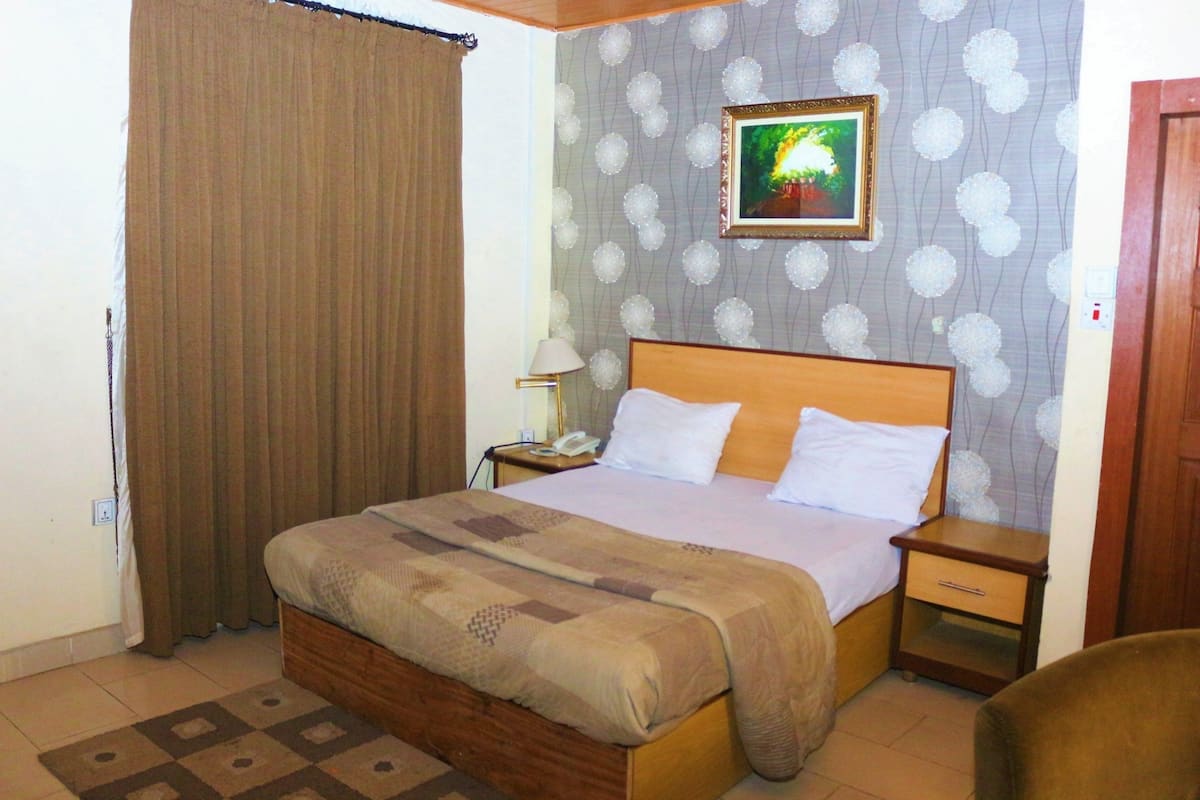 A bedroom with a bed, nightstand, and a painting on the wall.