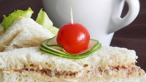 A sandwich with a cherry on top, surrounded by lettuce and cucumber slices, on a white plate. - Hotel Icon Limited (Calabar)