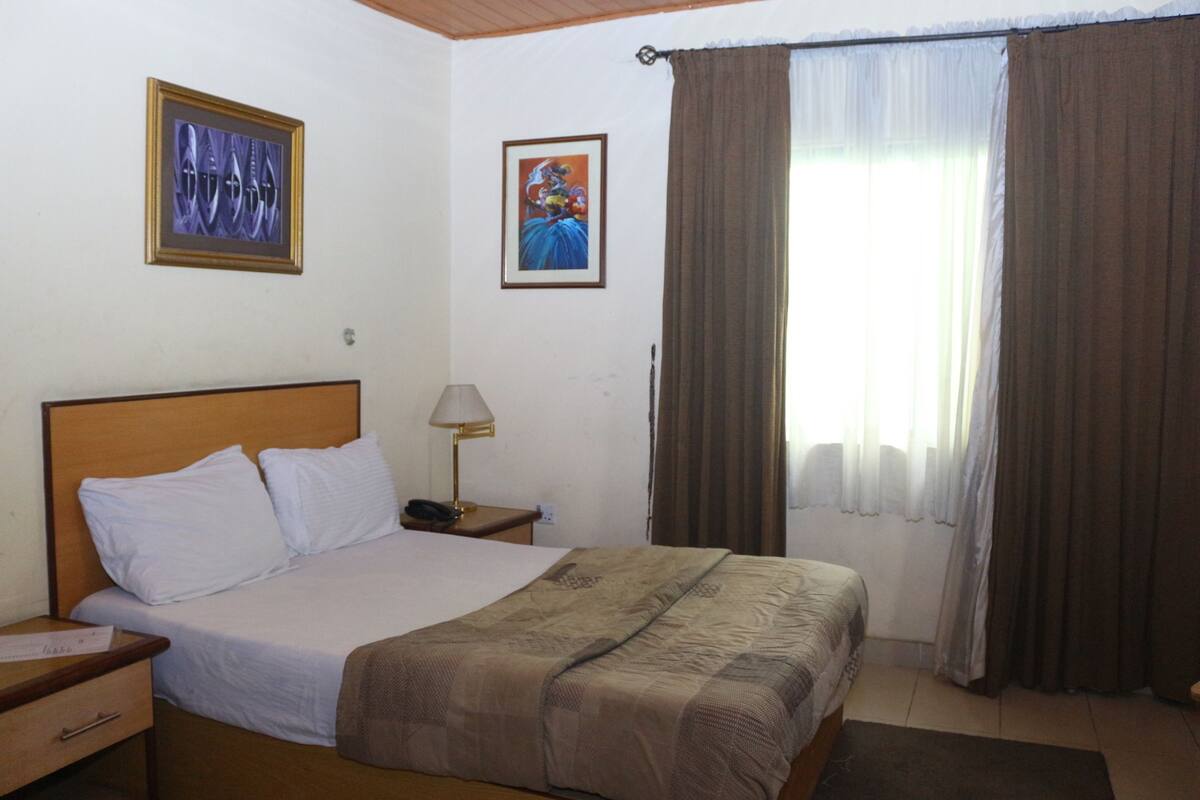 A hotel room with a bed, a nightstand, a lamp, and two framed pictures on the wall.