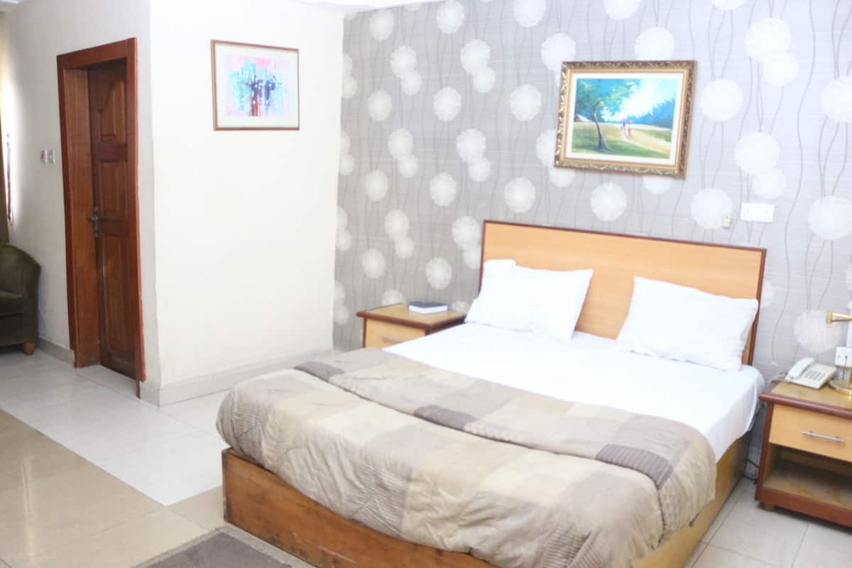 A bedroom with a bed, a nightstand, a wooden door, and a wall with a patterned wallpaper.