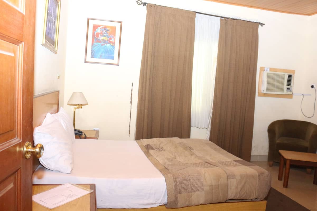 A hotel room with a bed, a chair, a lamp, and a picture on the wall.