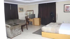A hotel room with a bed, a sofa, a desk with a computer, a chair, and a fan. - Hotel Icon Limited (Calabar)