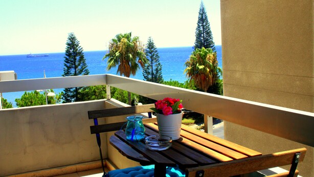 A balcony with a wooden table, a white vase with red flowers, and a clear glass pitcher. - Seventh Sea (Limassol)