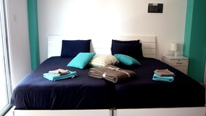A neatly made bed with a dark blue bedspread, two teal pillows, and a striped pillow. There are folded towels on the bed. - Seventh Sea (Limassol)