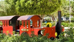 A miniature train set in a park with trees and playground equipment in the background. - Seventh Sea (Limassol)