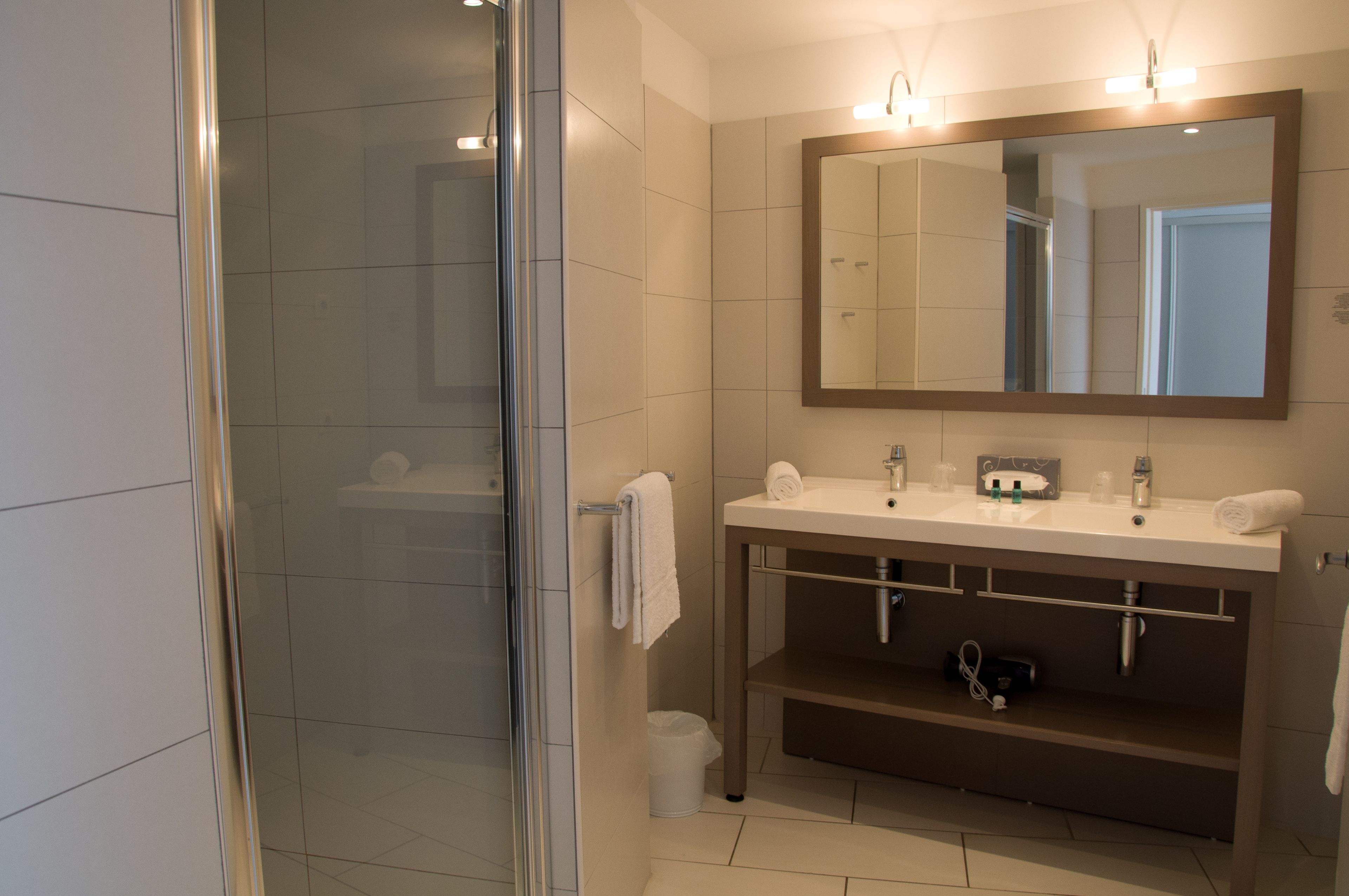 Un baño moderno con cabina de ducha de vidrio, un espejo grande y un tocador con dos lavabos y un perchero para toallas.