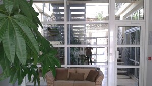 Een woonkamer met een geweven bank, een bijzettafeltje met decoratieve objecten, en grote ramen met uitzicht op het exterieur.