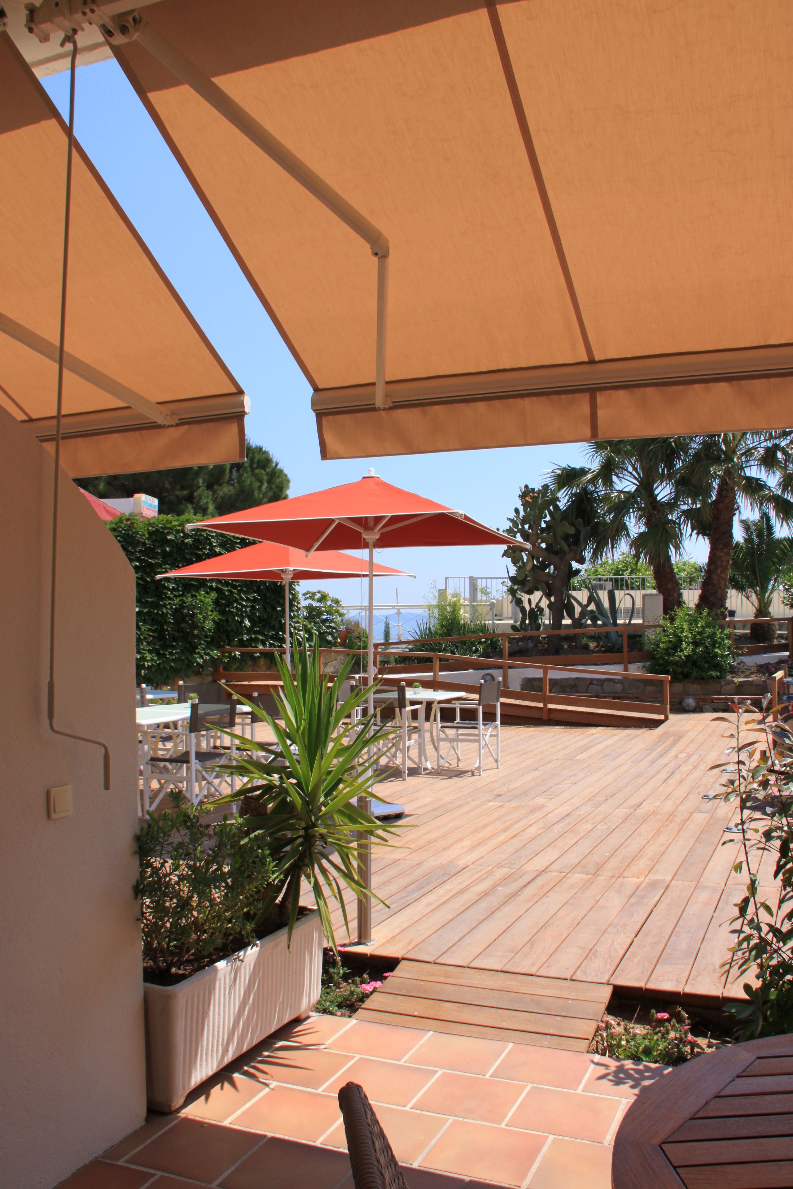 Une terrasse extérieure avec un sol en bois, des parasols rouges et des sièges d’extérieur.