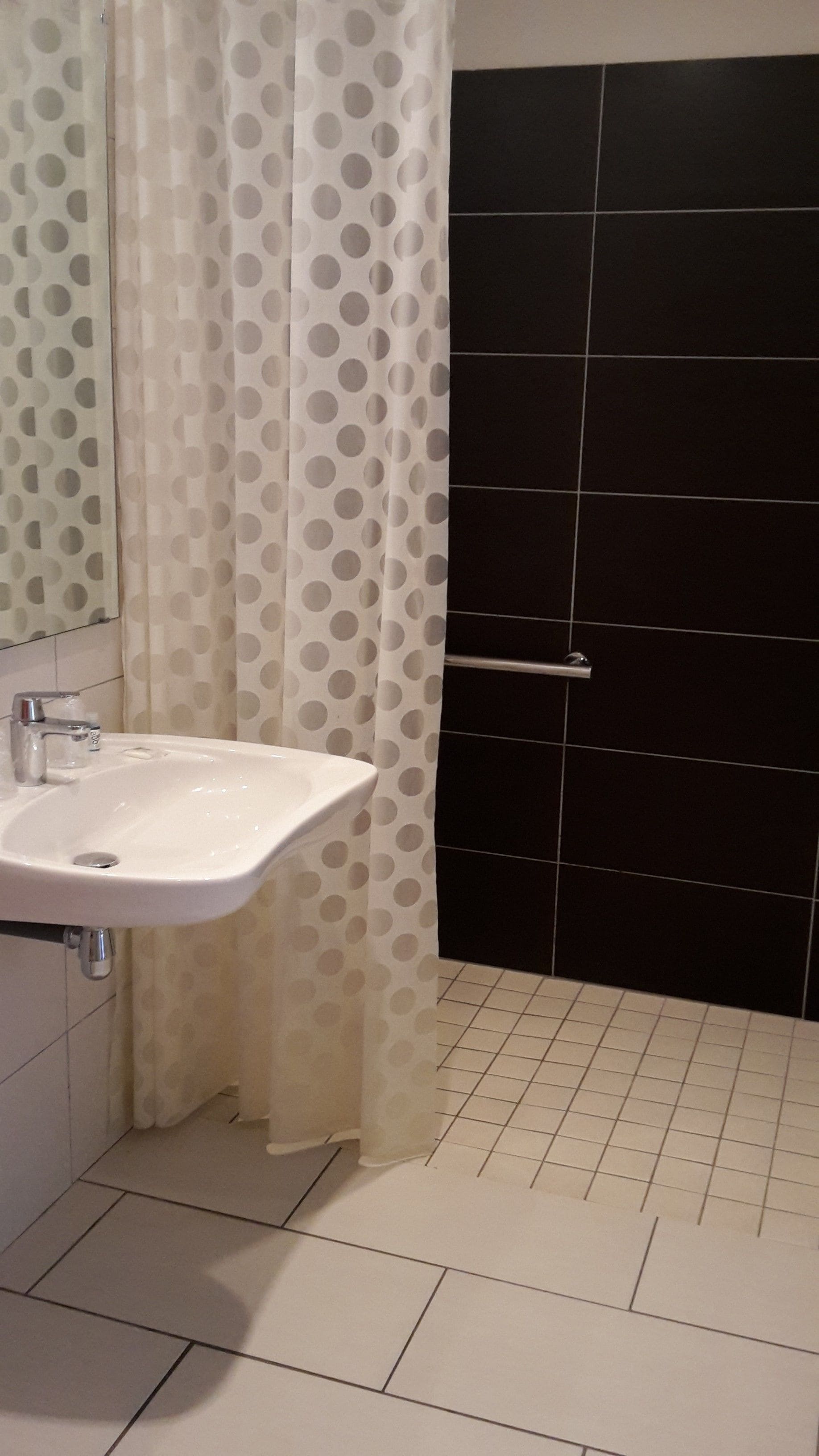 A bathroom with a white sink, a mirror, and a shower area with black tiles.
