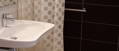 A bathroom with a white sink, a mirror, and a shower area with black tiles.
