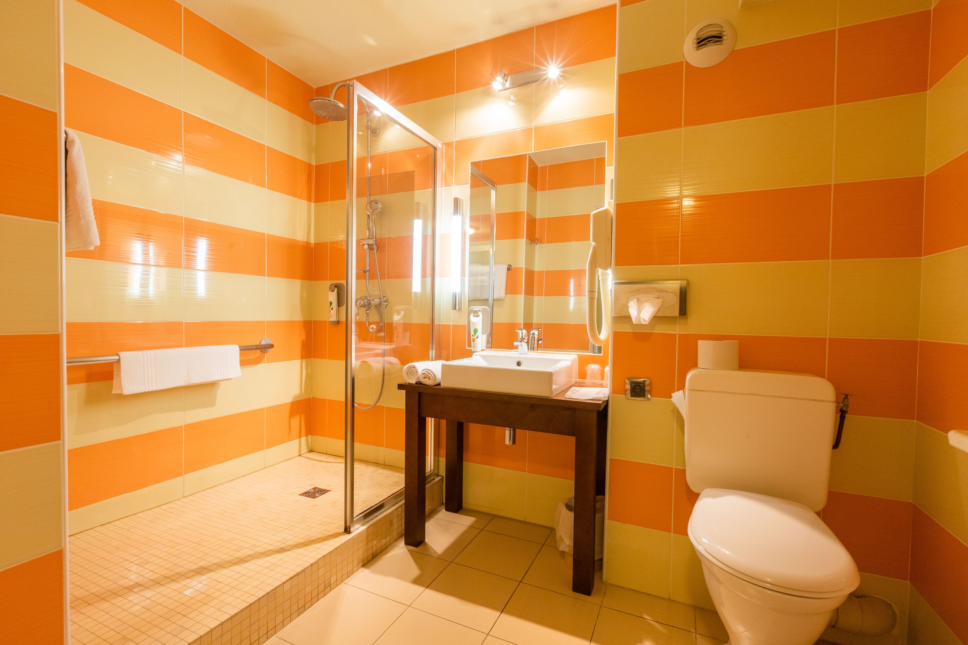 A bathroom with orange and white striped tiles, a glass shower enclosure, a sink with a mirror, and a toilet.