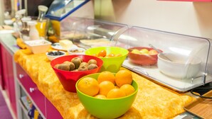 Un bufé con distintos alimentos en recipientes de colores, como frutas y nueces, sobre un mantel amarillo.