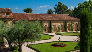 Un patio con un edificio de piedra, césped impecable y diversos árboles.