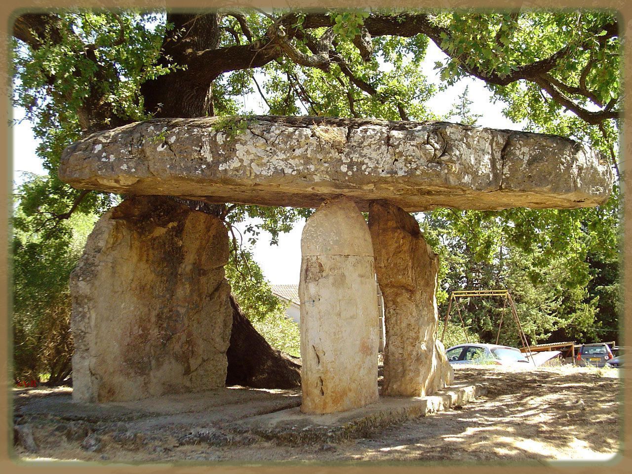 A stone structure with a flat top, supported by four pillars, surrounded by trees.