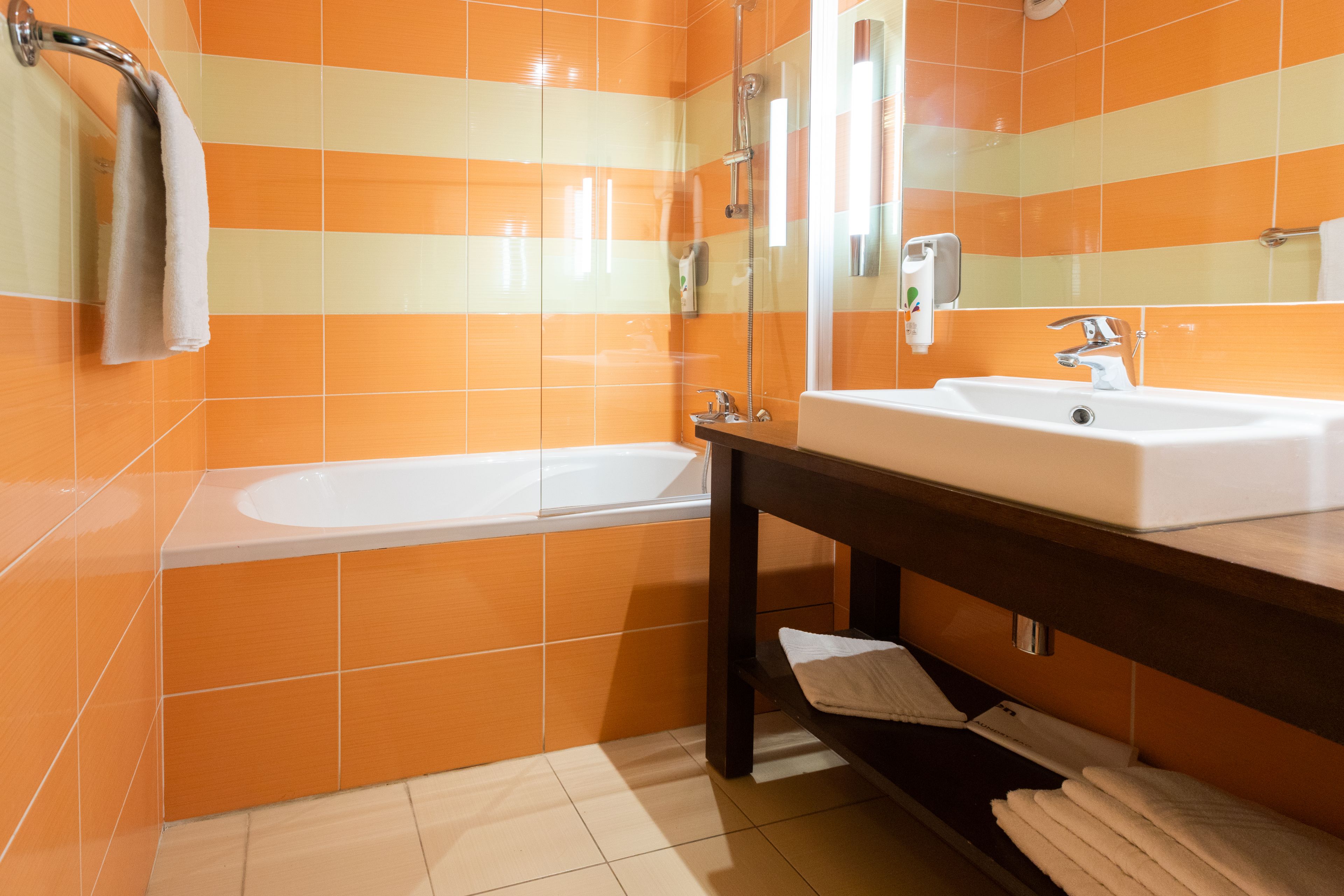 A bathroom with orange and beige tiles, a white bathtub, a sink, and a mirror.