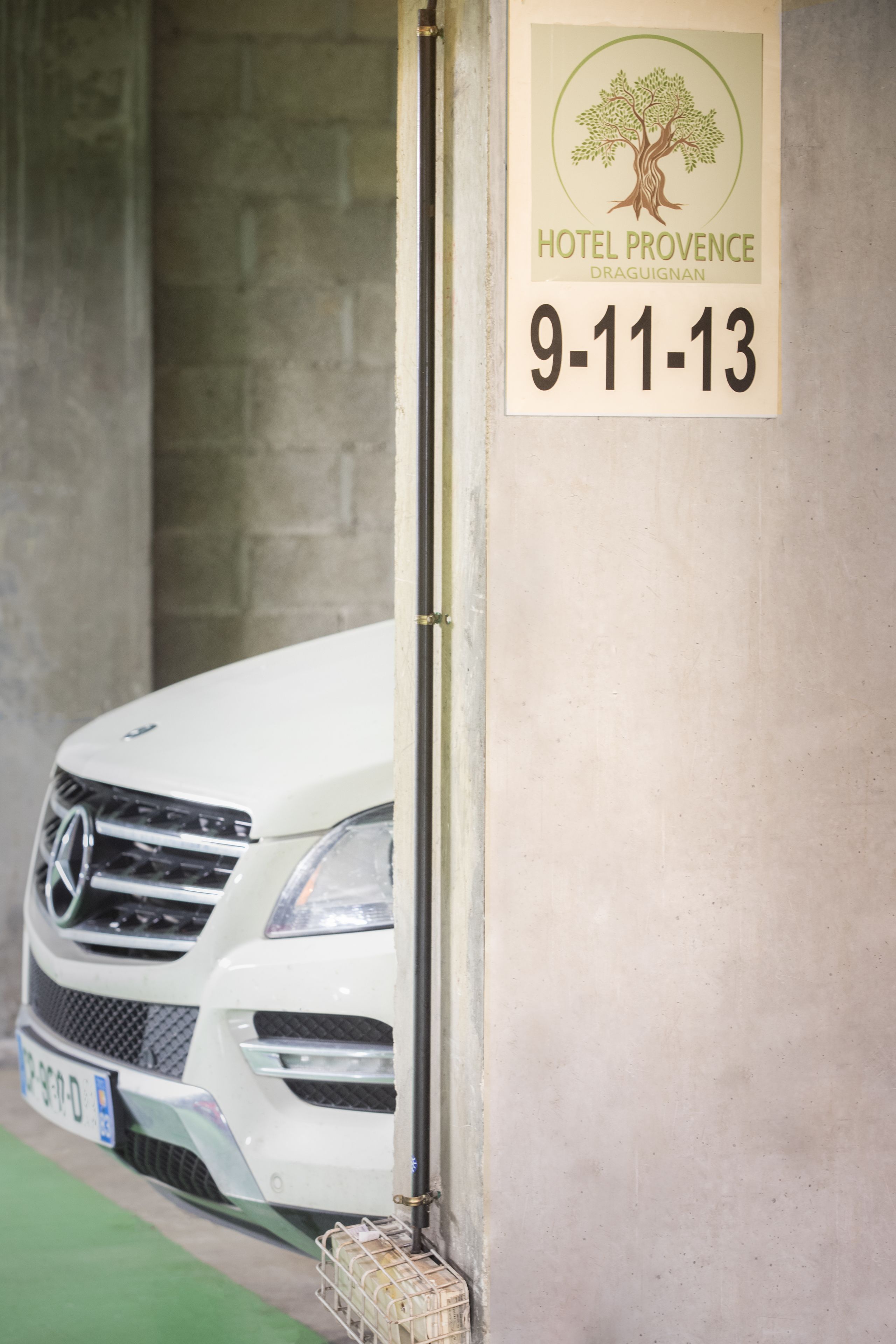 A white car parked in a garage with a sign indicating Hotel Provence Draguignan and dates 9-11-13.