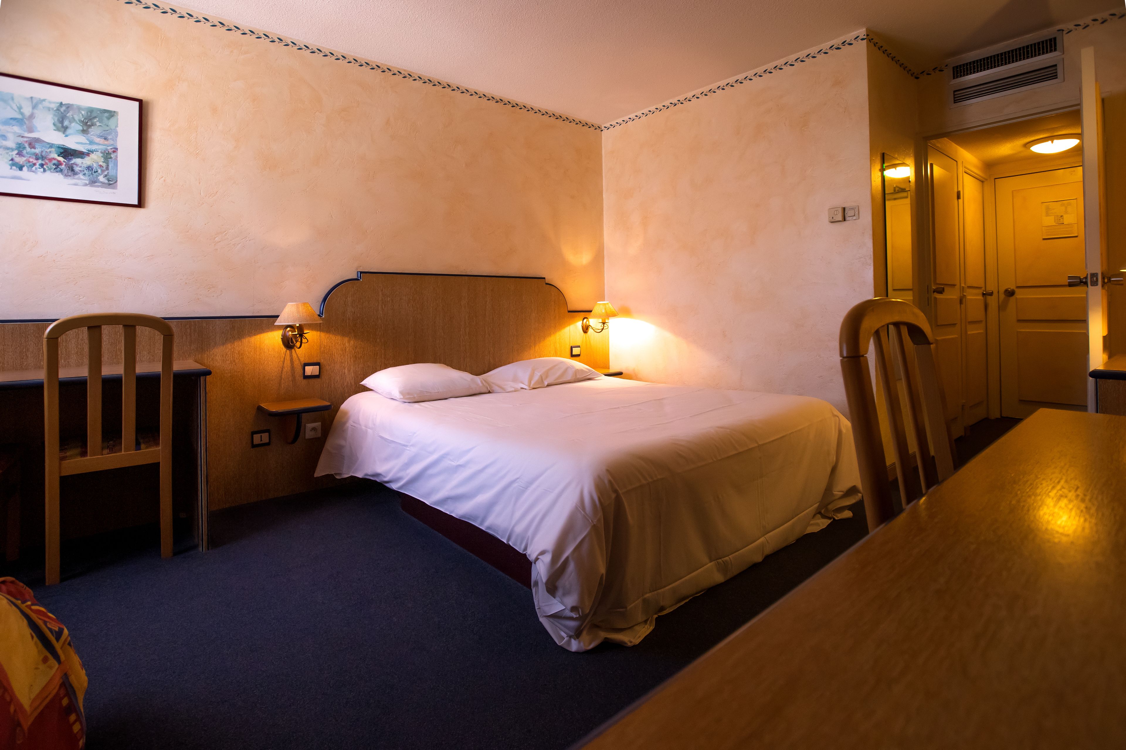 Et hotelværelse med en seng, to sengeborde, et skrivebord og en stol.