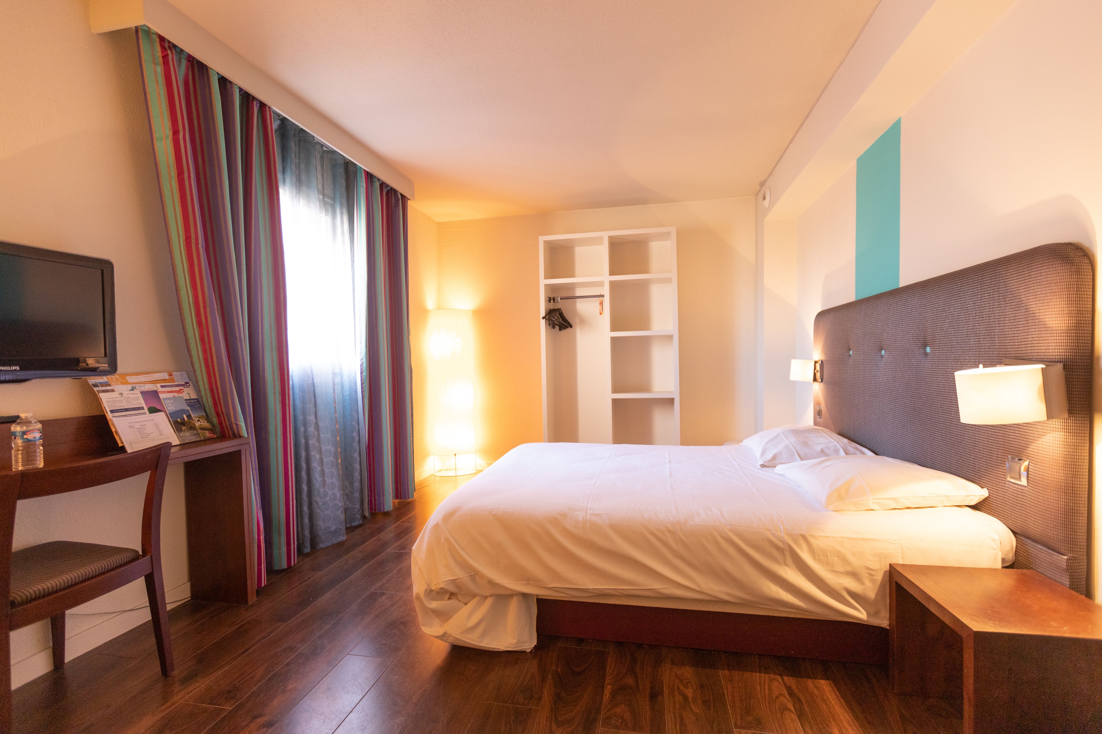 Una habitación de hotel con cama, escritorio, silla, televisor y armario.