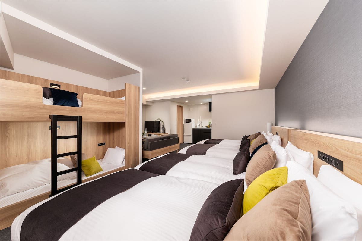 A modern hotel room with bunk beds, a kitchenette, and a bathroom.