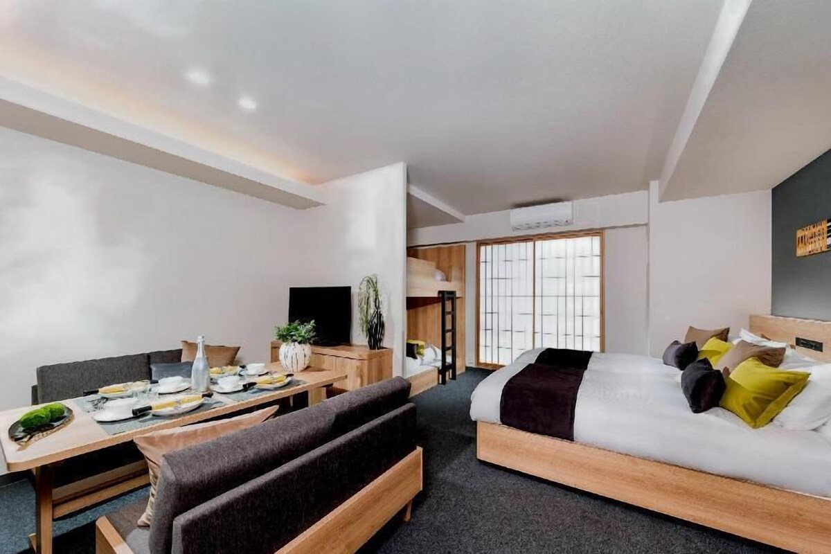 A modern hotel room with a bed, a dining table, a sofa, and a TV.