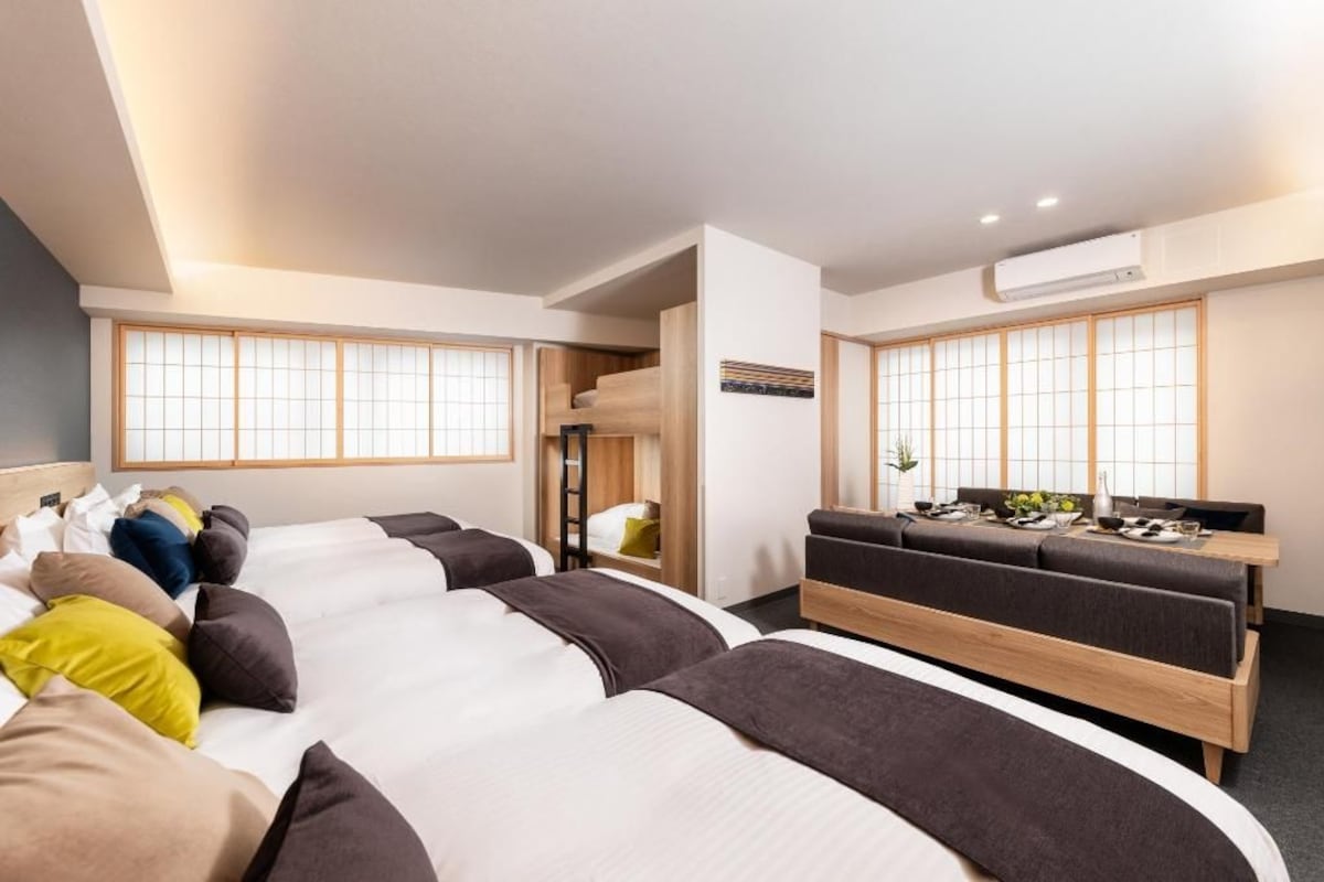 A hotel room with multiple beds, a dining area, and large windows with traditional shutters.