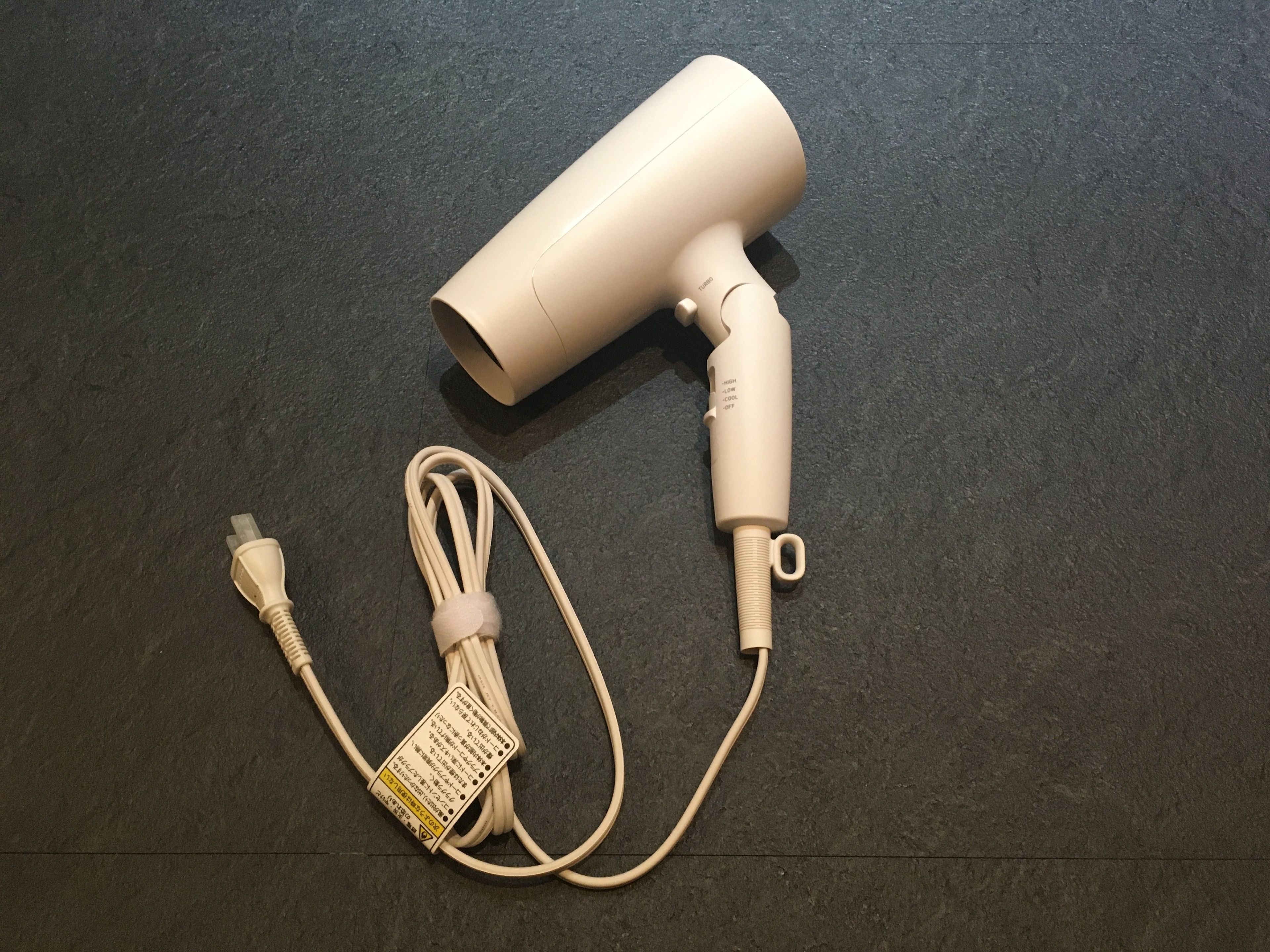 Un secador de pelo con cable y un adaptador de corriente sobre una superficie oscura.