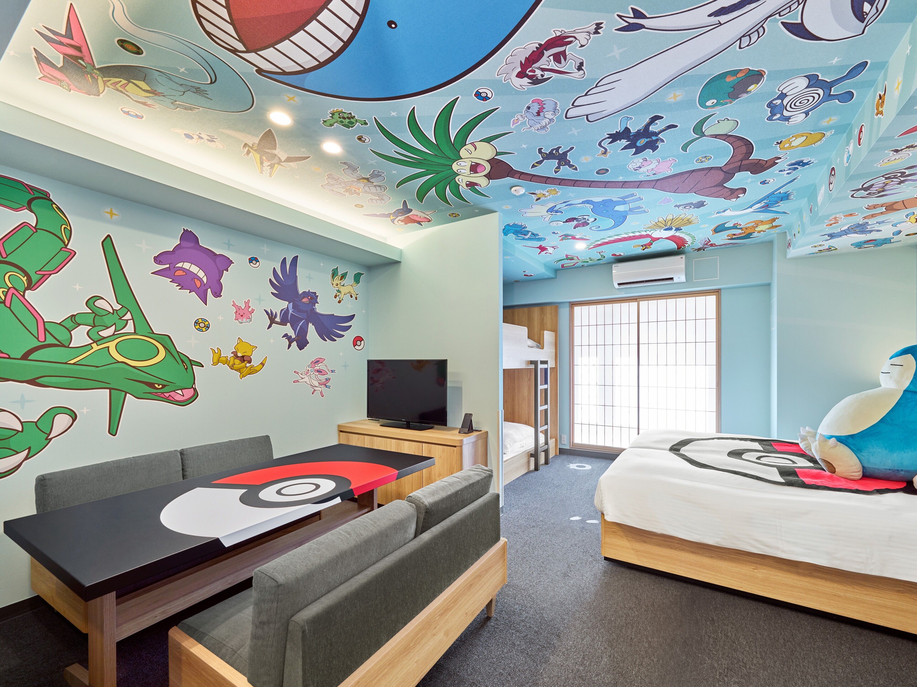A hotel room with a bunk bed, a flat-screen TV, a sofa, and a ceiling mural with various characters.