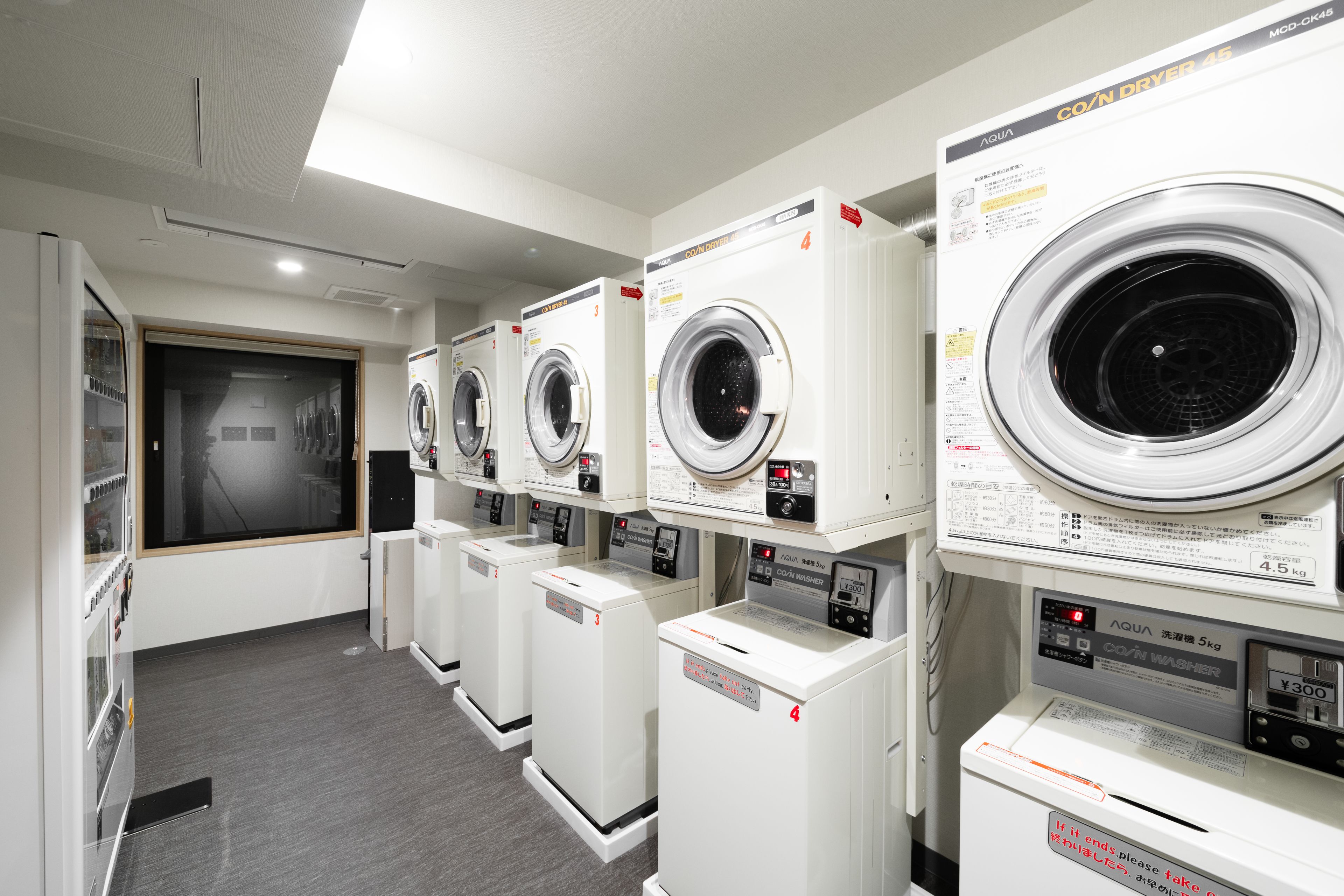 A row of white, front-loading washing machines in a commercial setting.