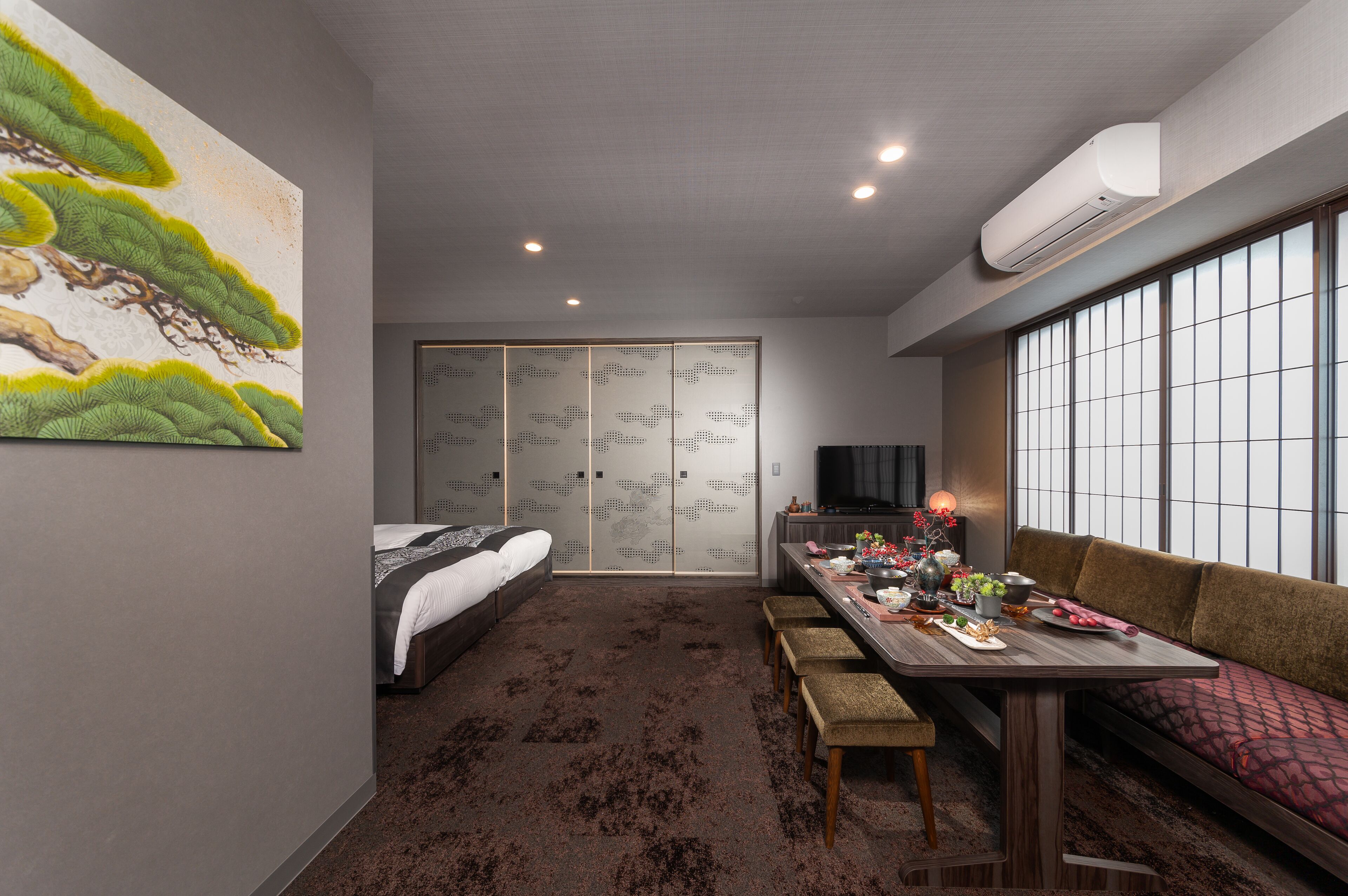 Ein kleines Hotelzimmer mit Bett, Esstisch mit Stühlen, einer Couch, einem Fernseher und einem großen Fenster.