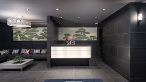A reception area with a dark color scheme, a reception desk, a sofa with patterned cushions, and a blue carpet with the hotel name. - MIMARU Tokyo Ginza East (Tokyo)