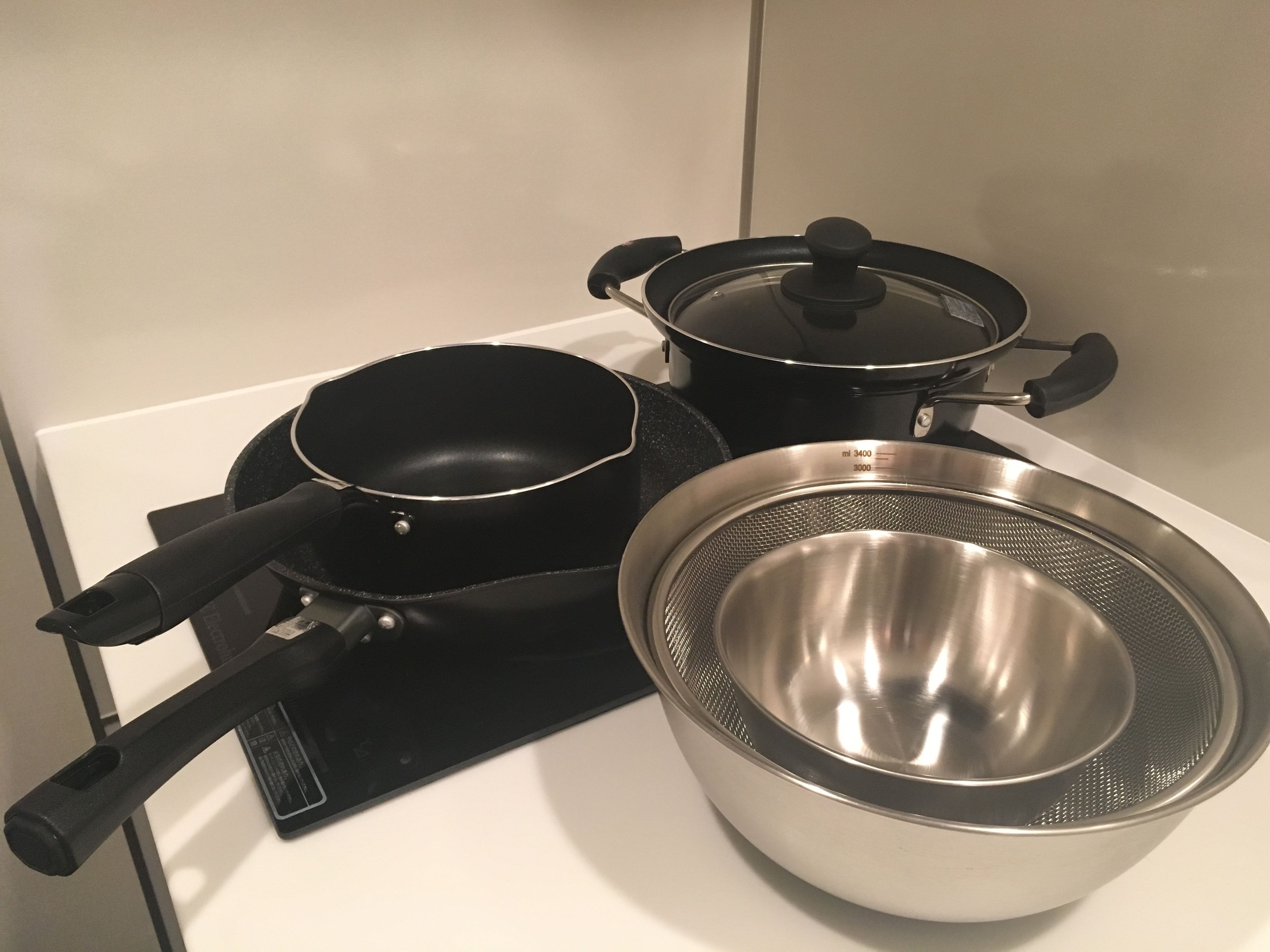 A kitchen with a stove, a frying pan, a pot with a lid, and a colander.