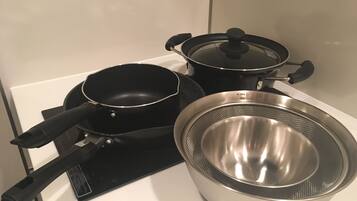 A kitchen with a stove, a frying pan, a pot with a lid, and a colander.