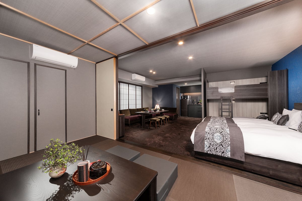 A modern hotel room with a large bed, a dining area, and a kitchenette.