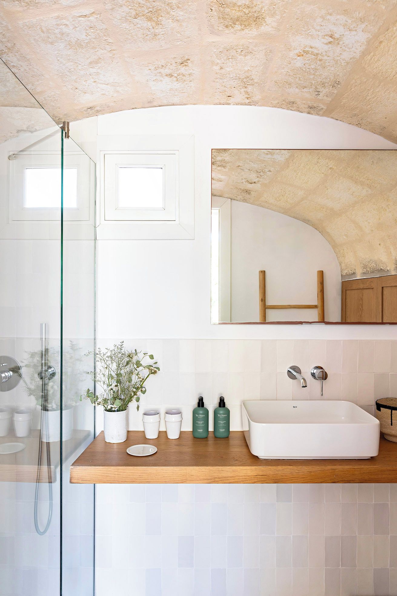 A modern bathroom with a glass shower enclosure, a wooden countertop, and a large mirror above a sink.