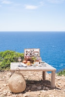 Un coin pique-nique aménagé avec un panier en osier, une table en bois et une vue sur la mer.