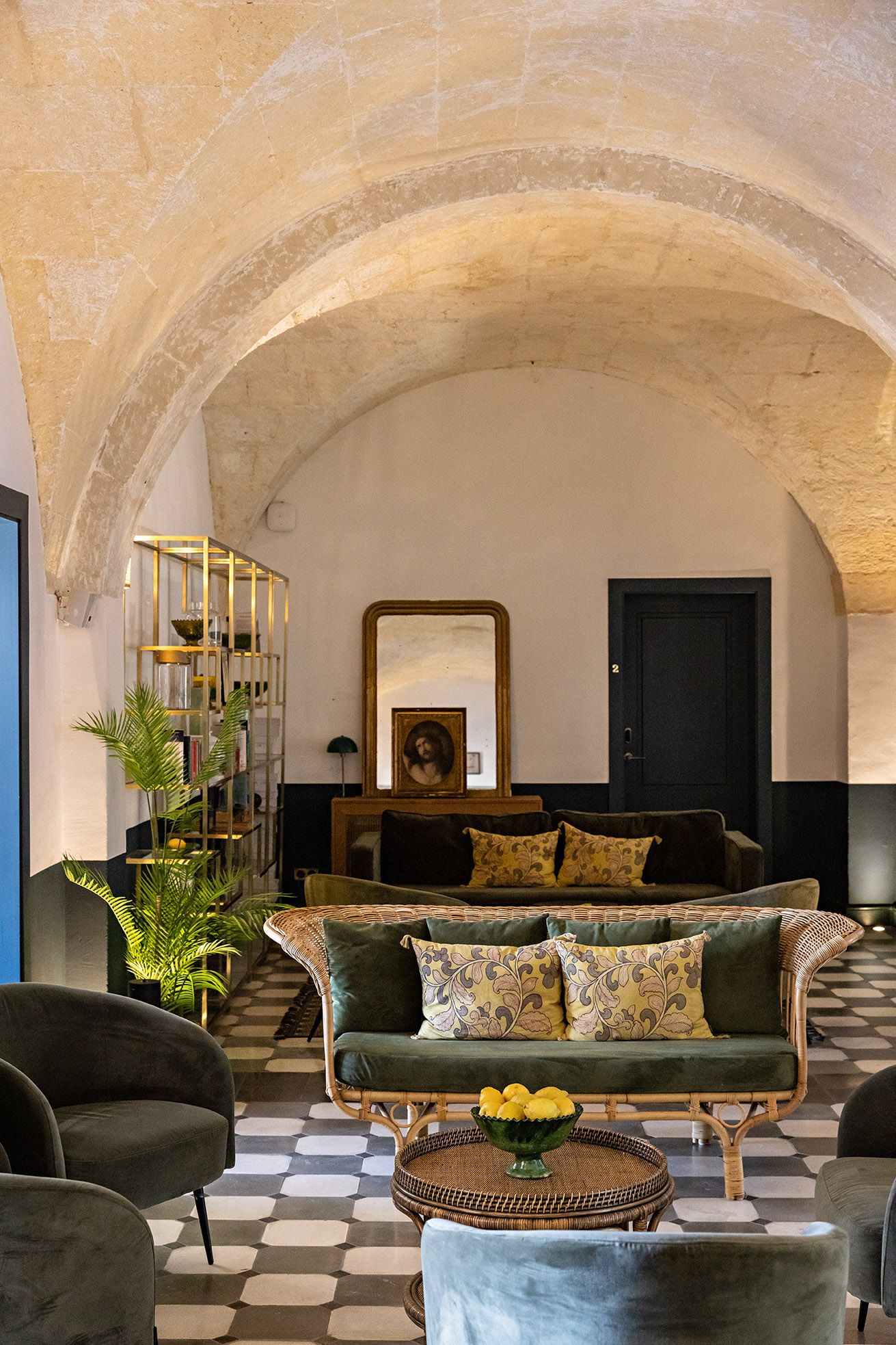 Una sala de estar acogedora con un sofá verde, una mesa de centro con fruta amarilla y una estantería con objetos decorativos.