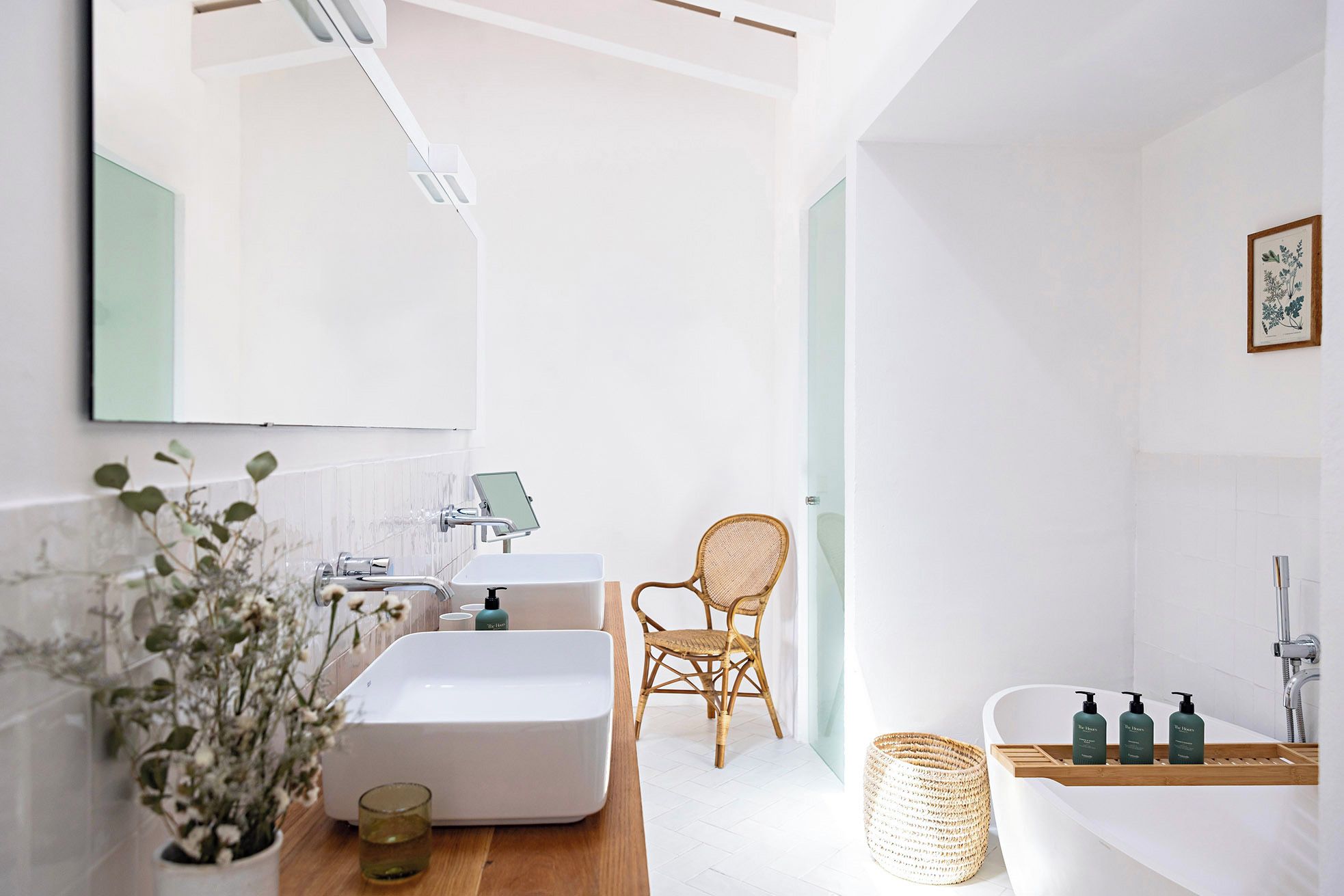 Ein modernes Badezimmer mit einem großen Spiegel, zwei Waschbecken, einer Badewanne und Korbmöbeln.