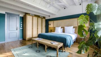 A bedroom with a bed, wooden wardrobe, bench, and a large plant.