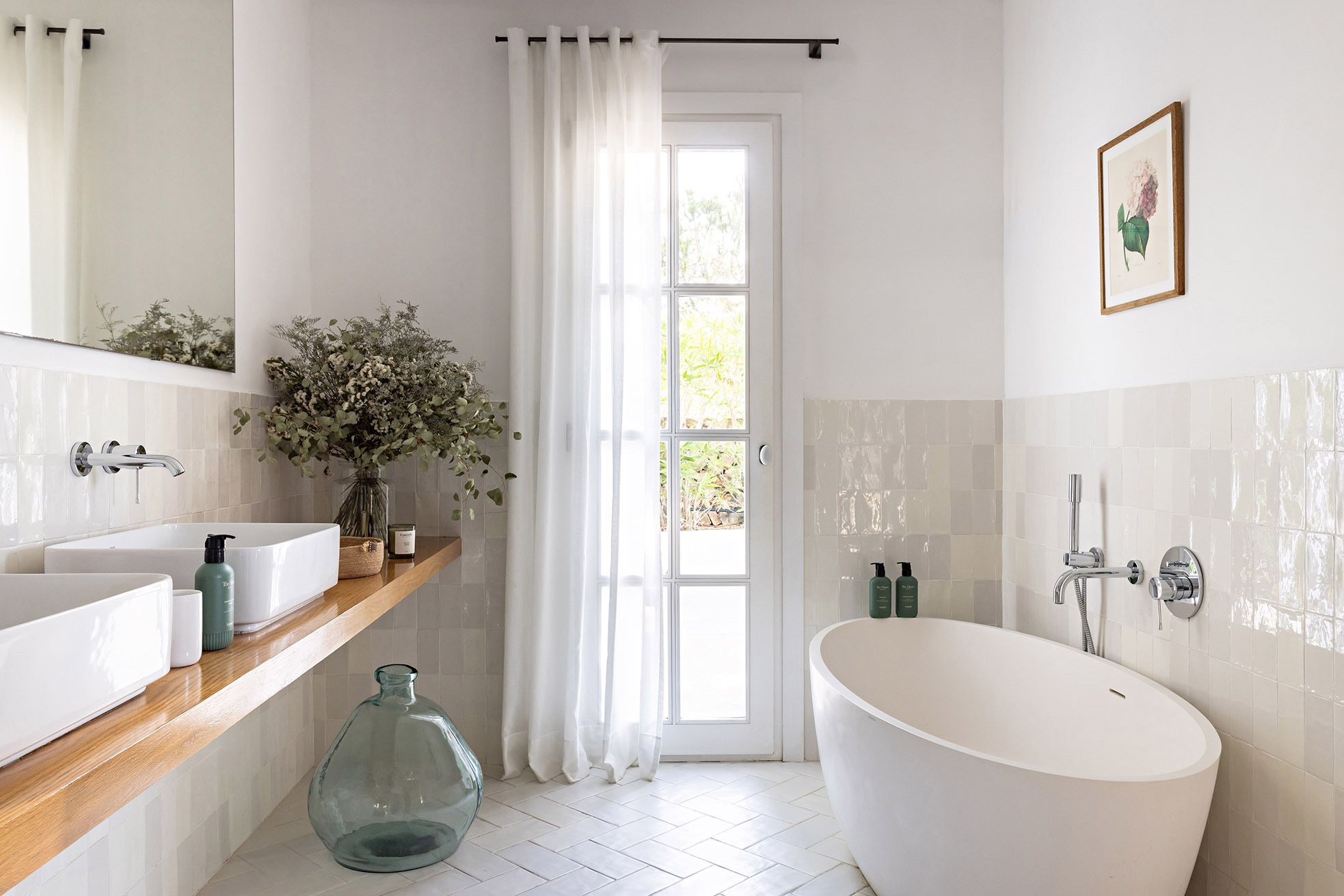 Un baño con una bañera independiente, un espejo grande y un ventanal con vistas a la vegetación.