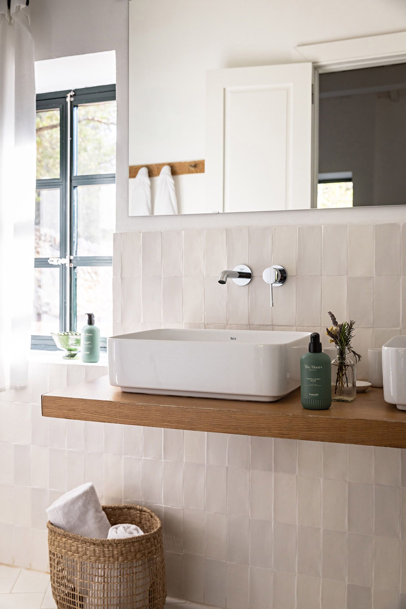 Un baño con un lavabo blanco, encimera de madera, espejo y ventana con cortinas.