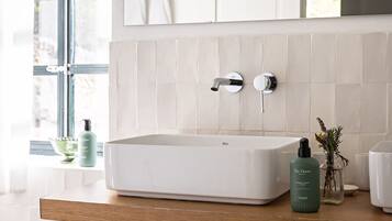 Un baño con un lavabo blanco, encimera de madera, espejo y ventana con cortinas.