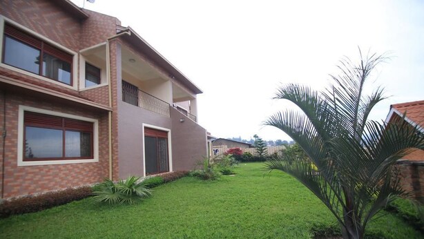 A two-story house with a well-maintained lawn and a palm tree. - UM Apartments (Kigali)