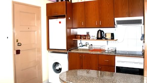 A compact kitchen with wooden cabinets, a built-in washing machine, and a microwave. - Happy Home 4 (Limassol)